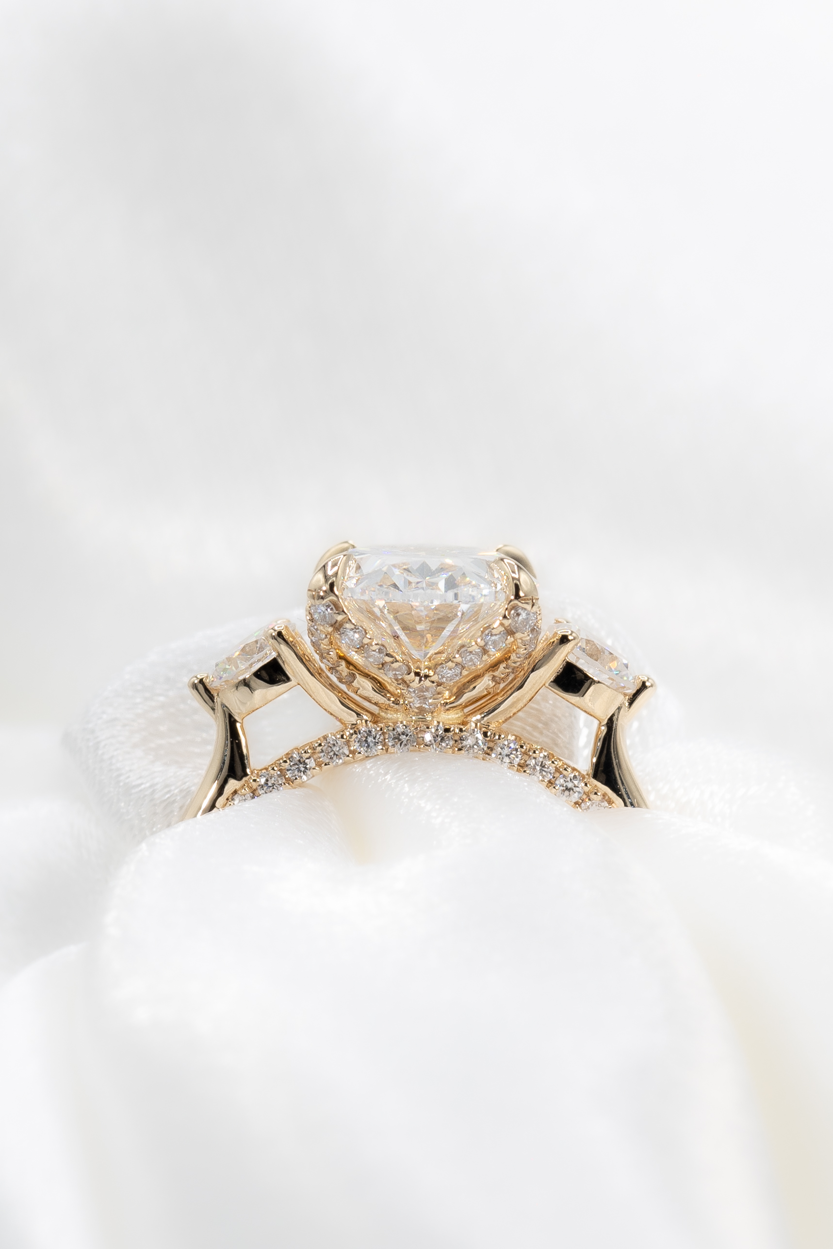 Gold engagement ring featuring a large triangular center diamond flanked by two smaller side diamonds and a diamond-studded band.