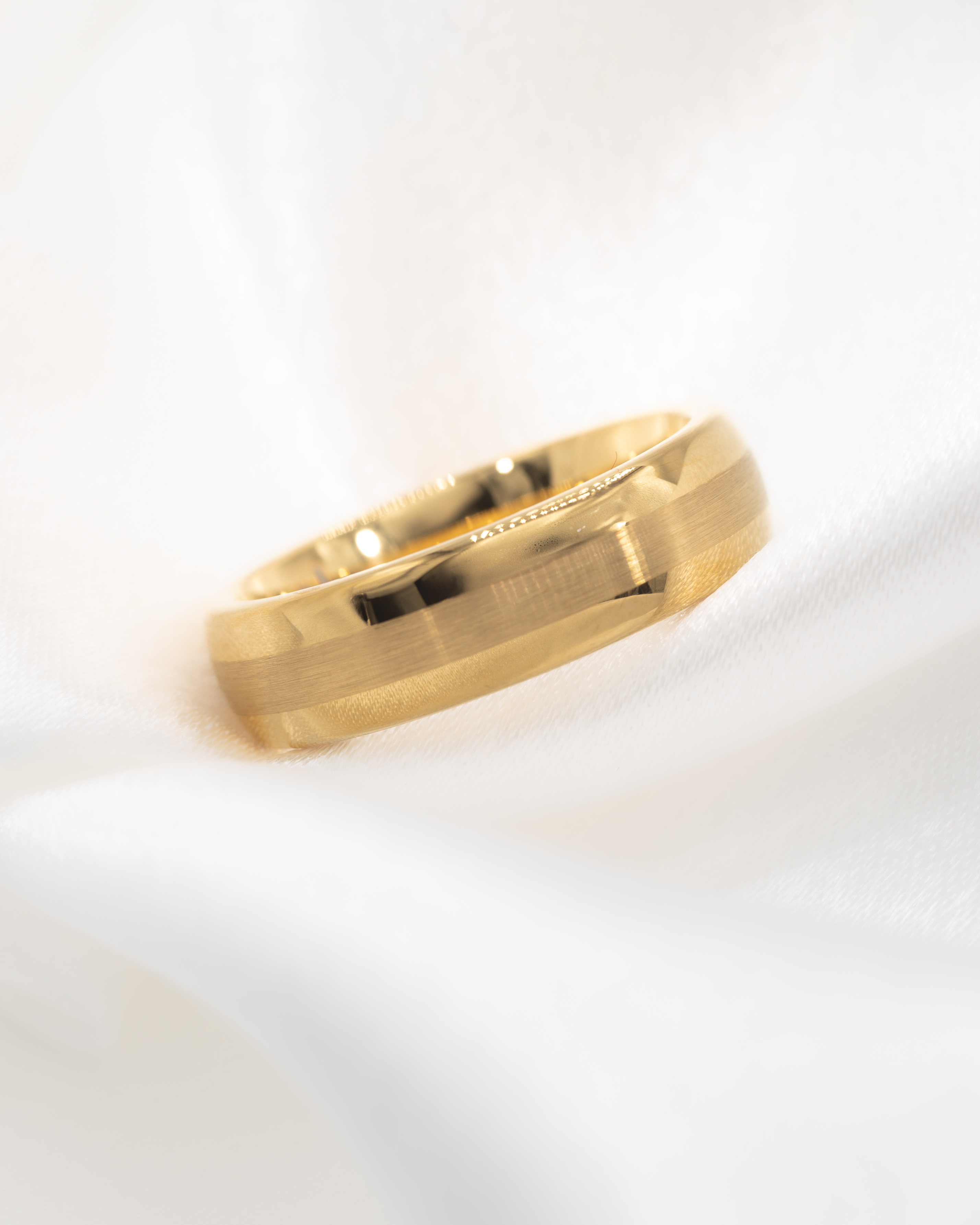 Close-up of a gold wedding band ring resting on soft white fabric.