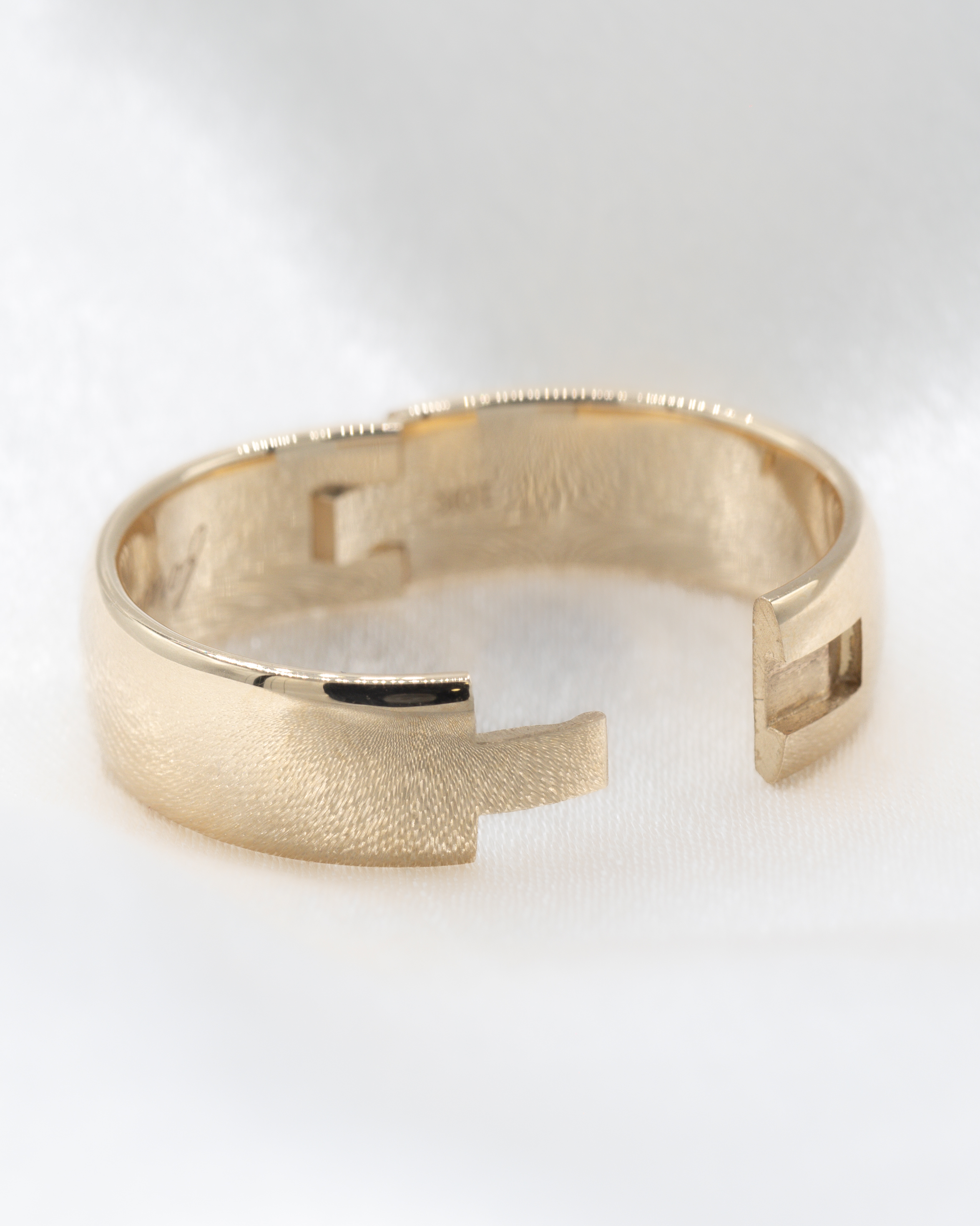 Close-up of a shiny gold hinged wedding band ring with an open design on a white surface.