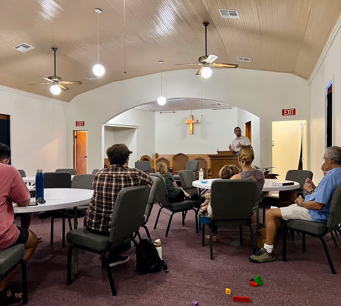 People sitting at circle tables listening to Rob Russell teach during a Questioning Christianity class at Restoration Community Church in Mandeville