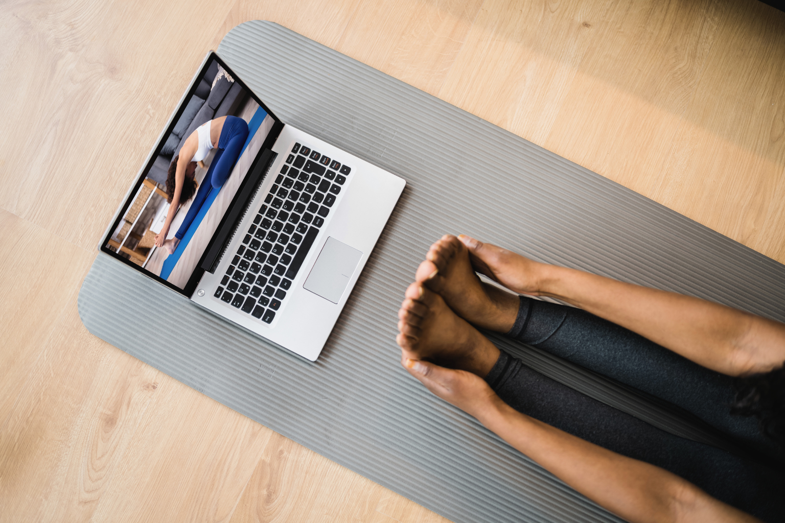 Person on a yoga mat following an online fitness class on a laptop, representing action and guided wellness coaching."
