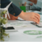 Personne écrivant sur du papier avec un stylo, avec un smartphone posé sur la table à côté et une plante en arrière-plan flou.
