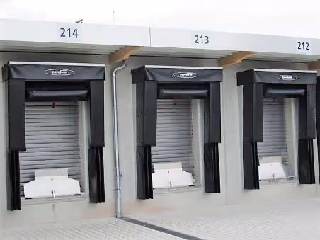 Drei geschlossene Lieferantentore mit schwarzen Schutzabdeckungen und den Nummern 214, 213 und 212 in einem Lagerhaus.