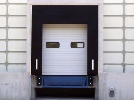 Geschlossene Ladetür an einer Lagerhauswand mit Schutzverkleidung aus schwarzem Material.