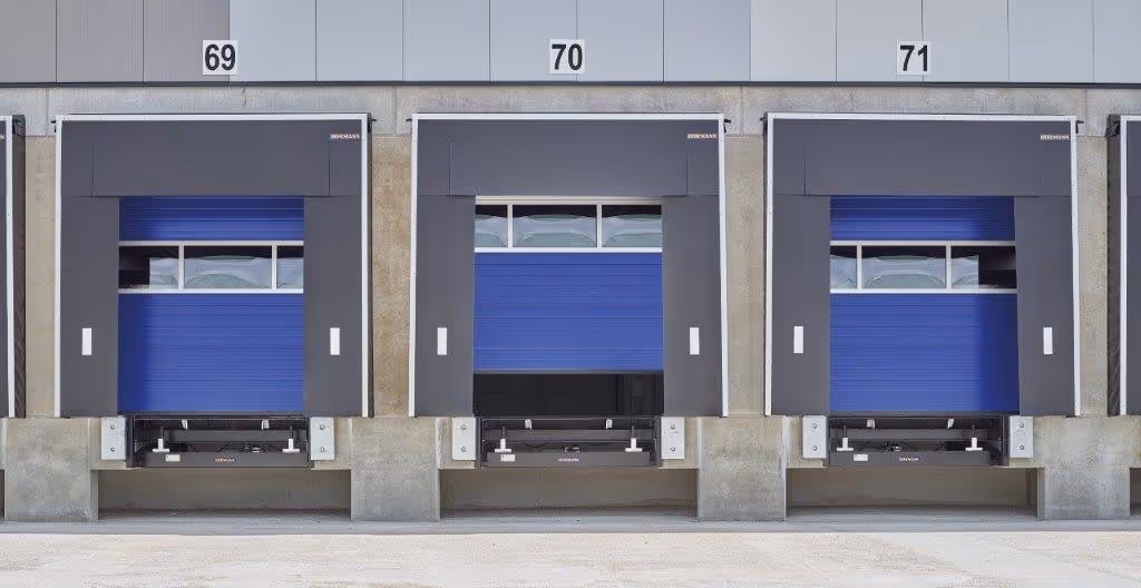 Drei blaue Laderampen mit schwarzen Pufferrahmen und Nummern 69, 70 und 71 an einer Lagerhausfassade.