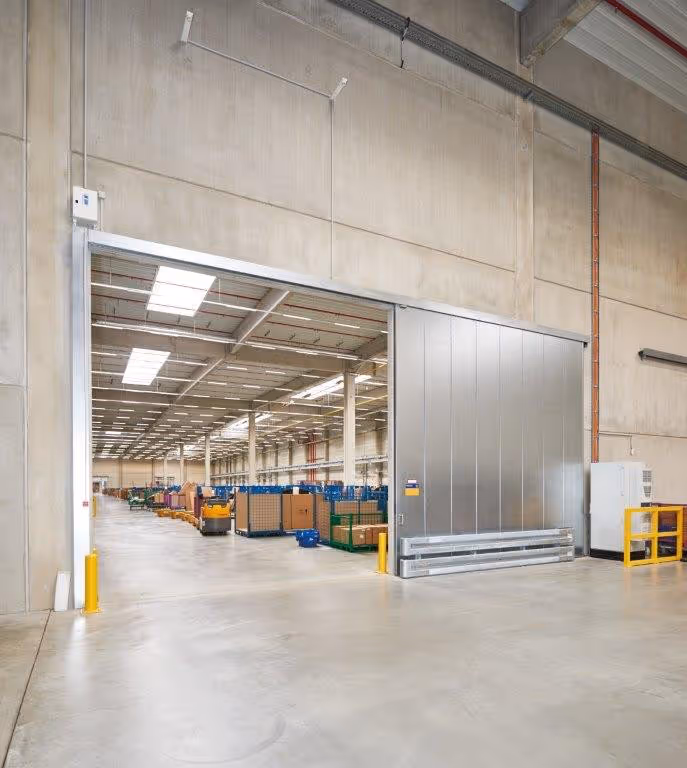 Großes automatisches Schiebetor aus Metall mit geöffnetem Zustand in einem Lagerhaus mit Regalen und Kartons.