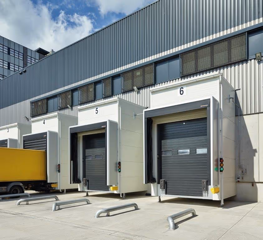 Lädtore Nummer 3 bis 6 an einem Gewerbegebäude mit angehängtem gelbem LKW an Tor 3.