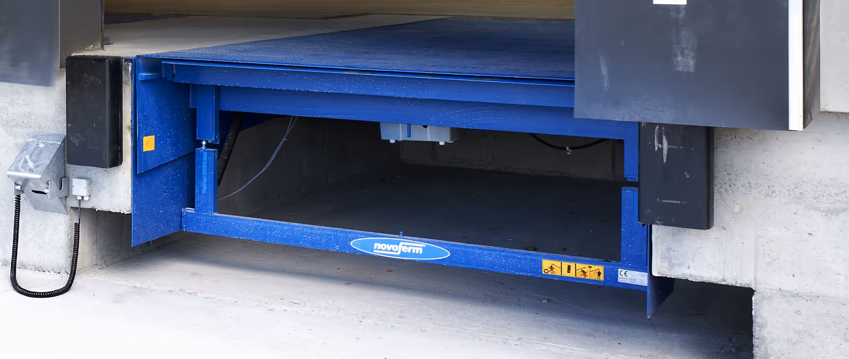 Blau lackierte Ladebordwand einer Laderampe mit Novoferm-Logo und Warnaufklebern.