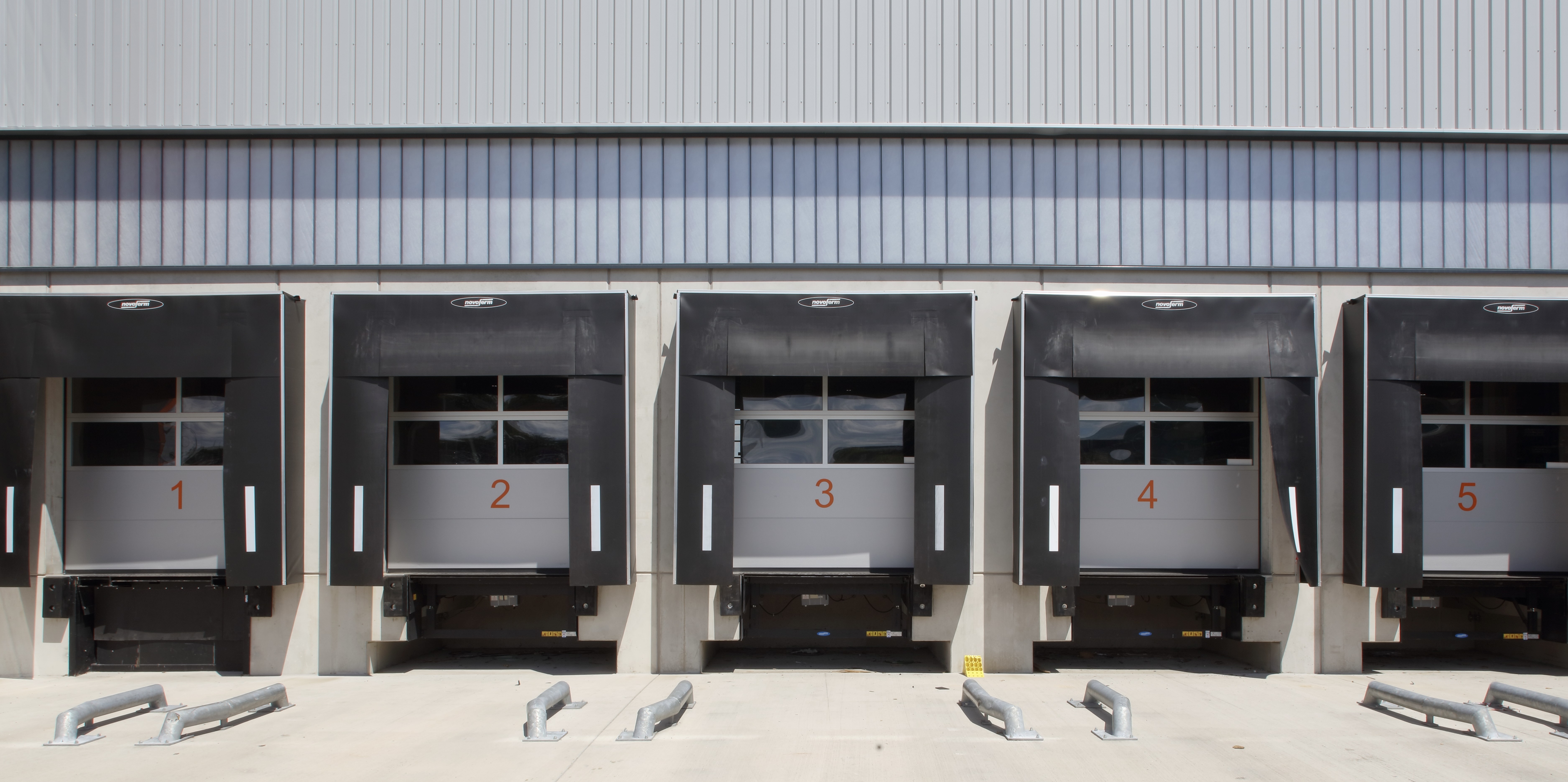 Fünf nummerierte Lagerladerampen mit schwarzen Schutzabdeckungen an einem Lagergebäude.