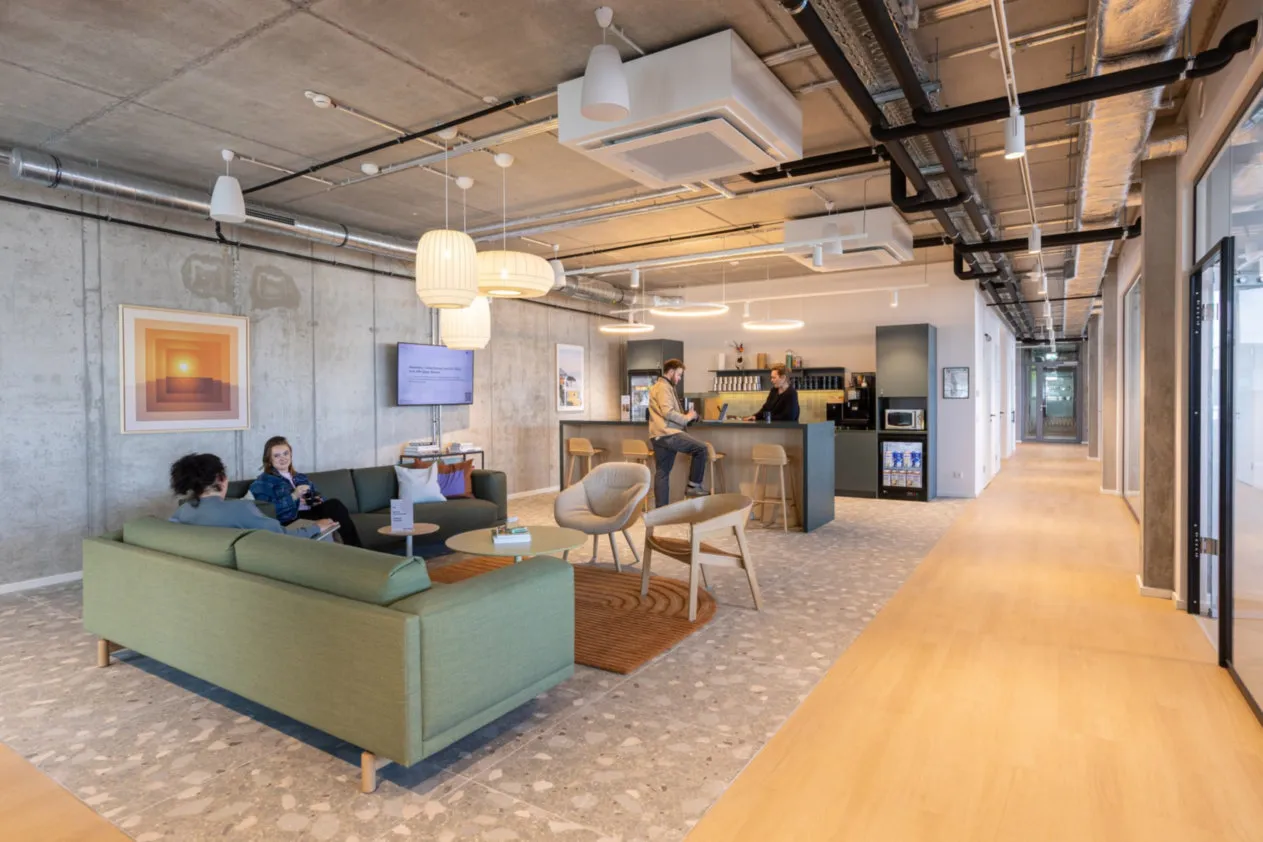 Modernes Coworking-Büro mit grüner Couch, Sitzbereich und Theke, an der Menschen miteinander sprechen.