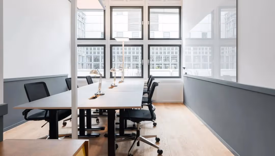 Arbeitsraum mit weißen Schreibtischen, schwarzen Netz-Drehstühlen, verchromten Schreibtischlampen, Rasterfenster