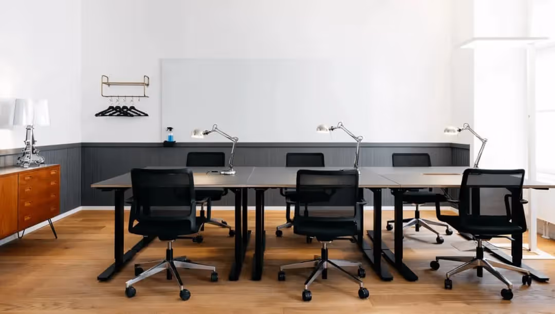Meetingraum mit Gemeinschaftstisch, schwarzen Mesh-Stühlen, grauen Tischplatten, Schreibtischlampen