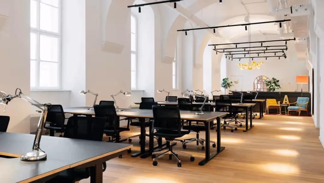 Coworking-Bereich mit Reihen schwarzer Schreibtische, hohen weißen Bogenfenstern, Track-Beleuchtung