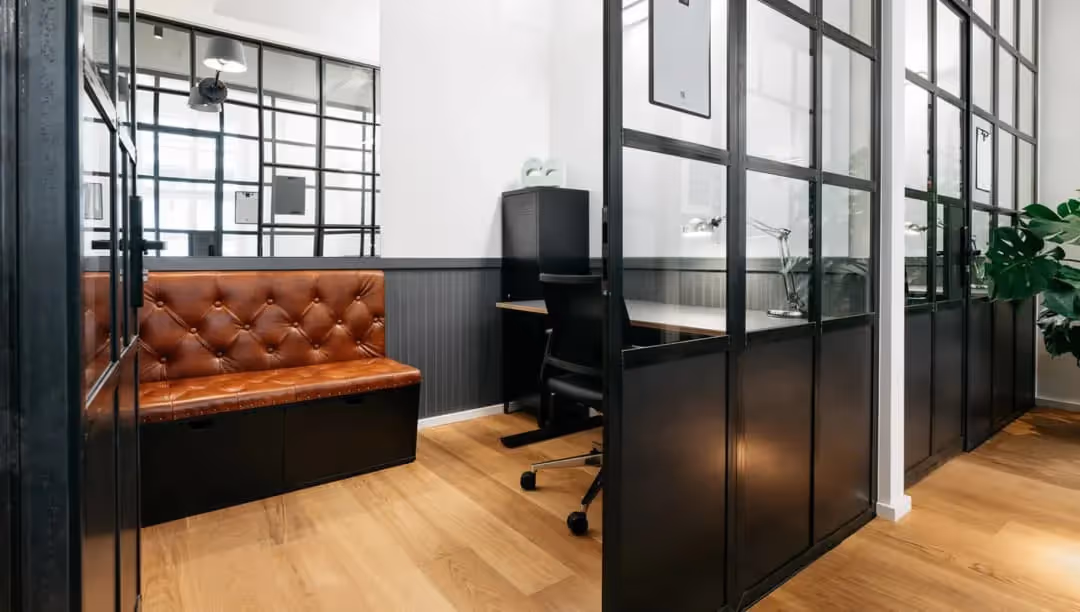 Kleines Büro mit schwarzen Stahl-Glastrennwänden, brauner gesteppter Lederbank, schwarzem Bürostuhl