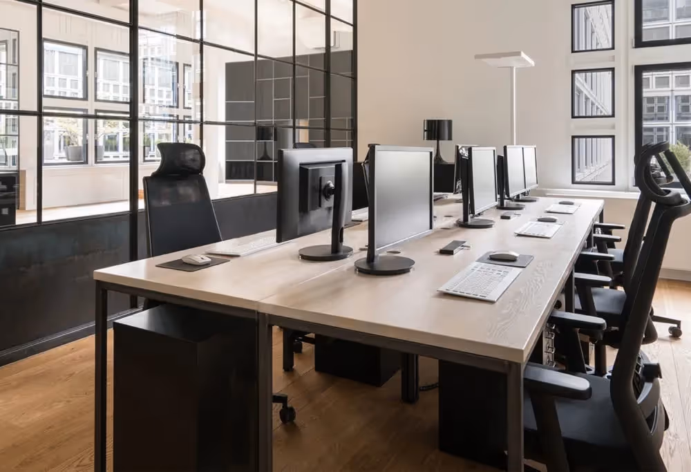 Open-Space-Arbeitsbereich mit langer Holz-Tischreihe, Monitoren, schwarzen ergonomischen Stühlen
