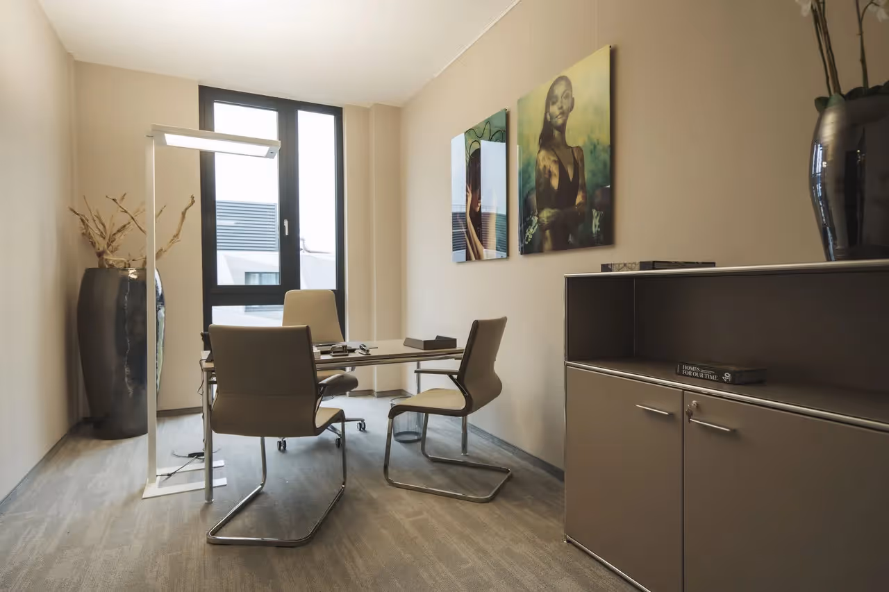 Helles Büro mit Glastisch, vier Stühlen, Stehlampe, zwei Wandbildern und großem Fenster. Schrank mit Dekoration.