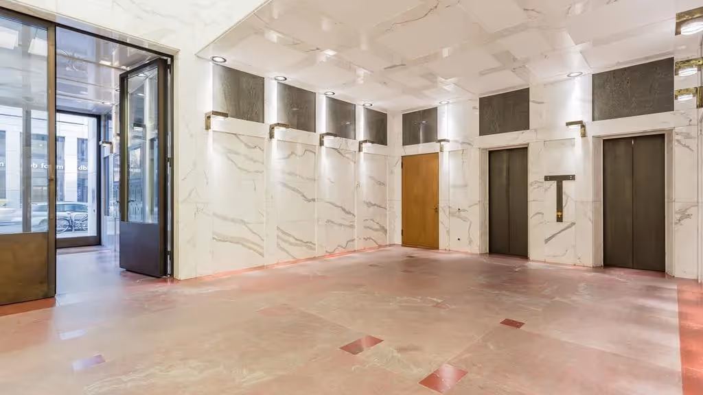 Marmorboden und -wände, zwei Aufzüge, Glastür, Deckenbeleuchtung, Holzdetails, moderner Empfangsbereich.