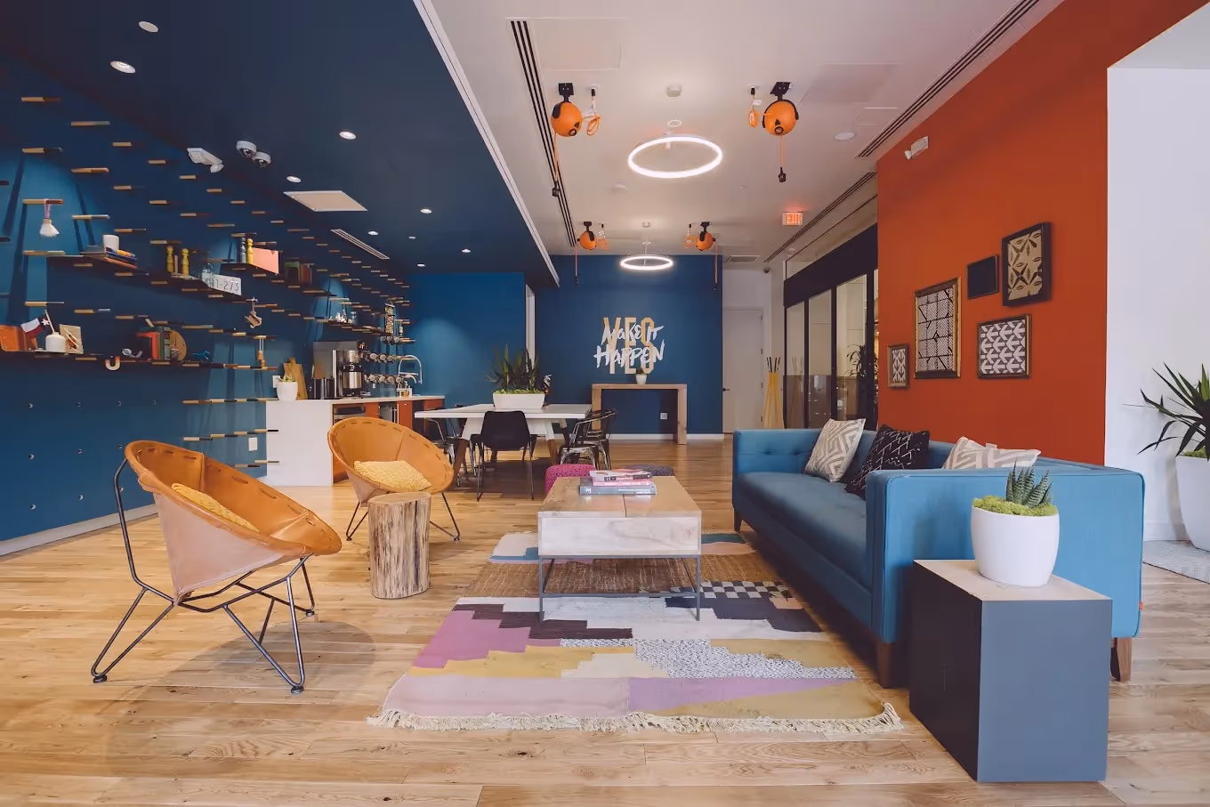 Blauer Raum mit Sofa, buntem Teppich, Regalen, Pflanzen, Holztisch, orangen Stühlen und dekorativen Wänden.