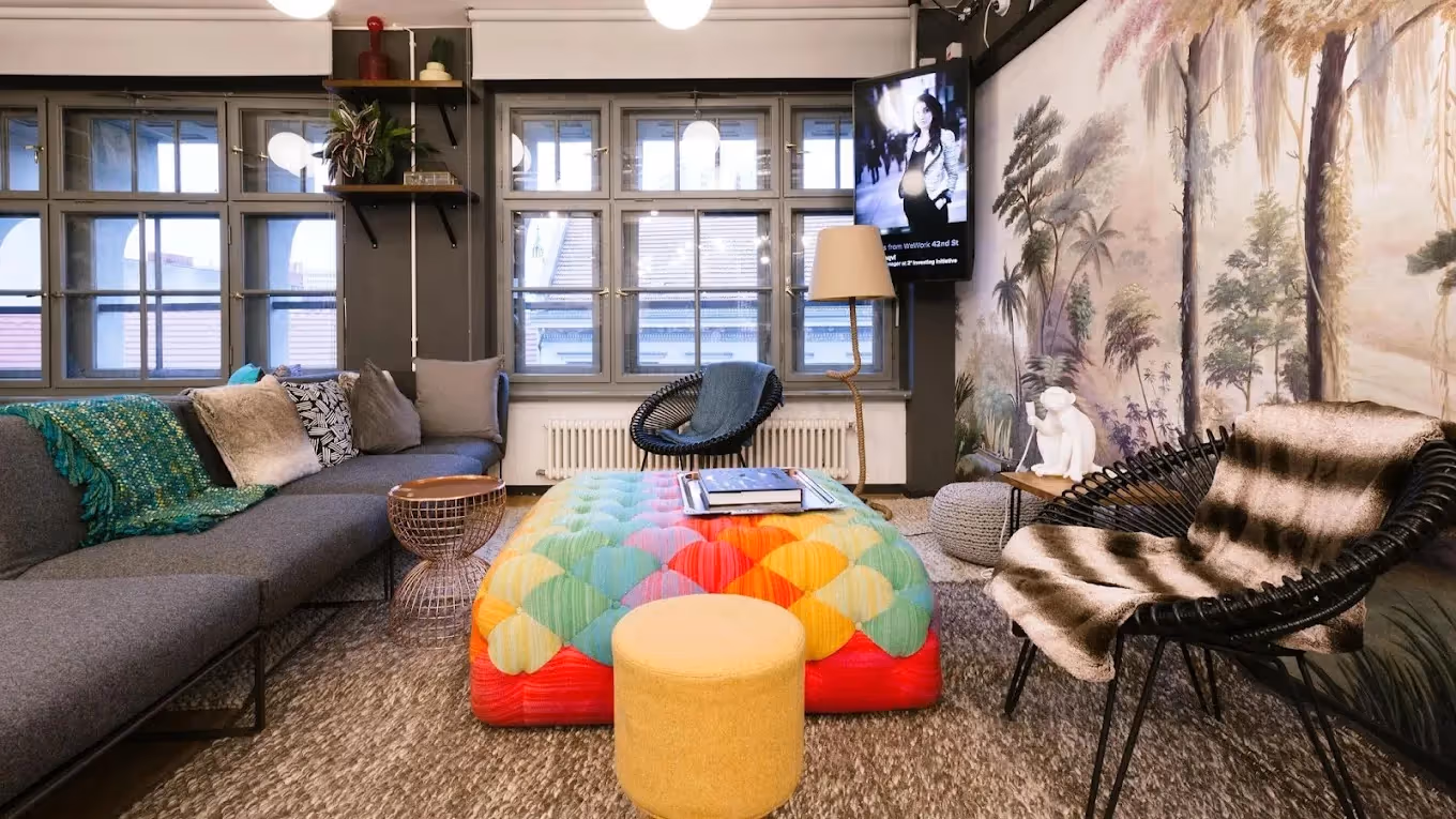 Bunte Lounge mit grauem Sofa, gemustertem Teppich, großen Fenstern, Wandgemälde und dekorativen Pflanzen.