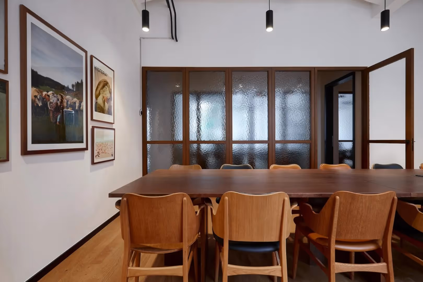 Holztisch mit Stühlen, Bilder an weißer Wand, Holztüren mit strukturiertem Glas, Hängeleuchten, Holzfußboden.