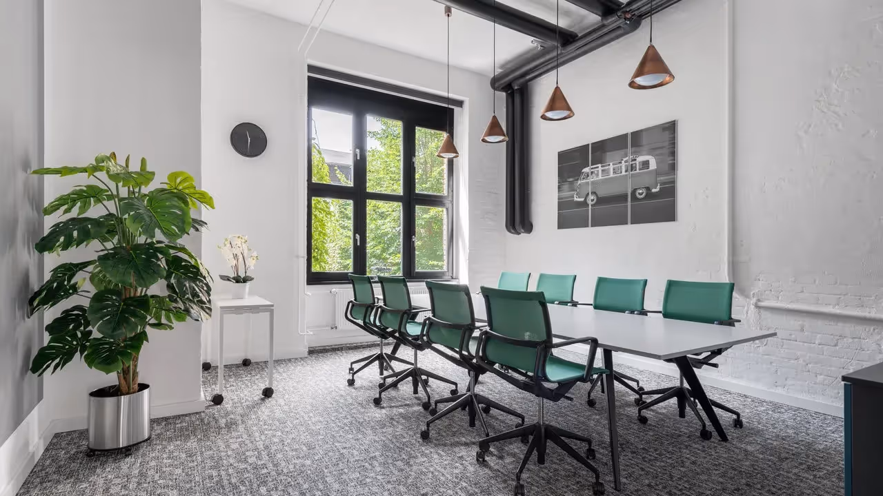 Konferenzraum mit grün gepolsterten Stühlen, weißem Tisch, Pflanzen, Fenster, Uhr, Kupferlampen und Wandbild.