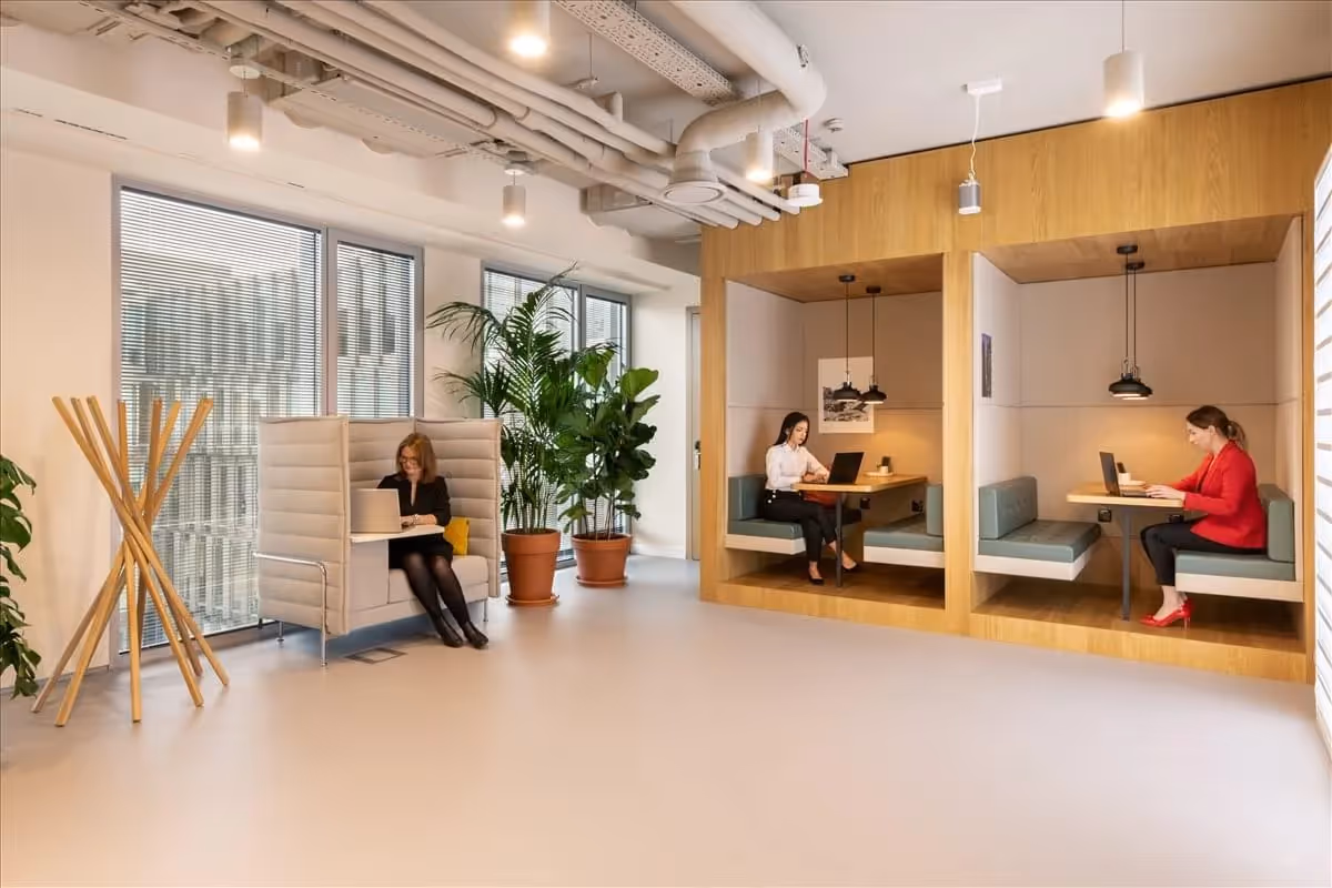 Zwei Personen arbeiten in gemütlichen Holznischen, eine weitere sitzt in einer gepolsterten Sitzgelegenheit, Pflanzen im