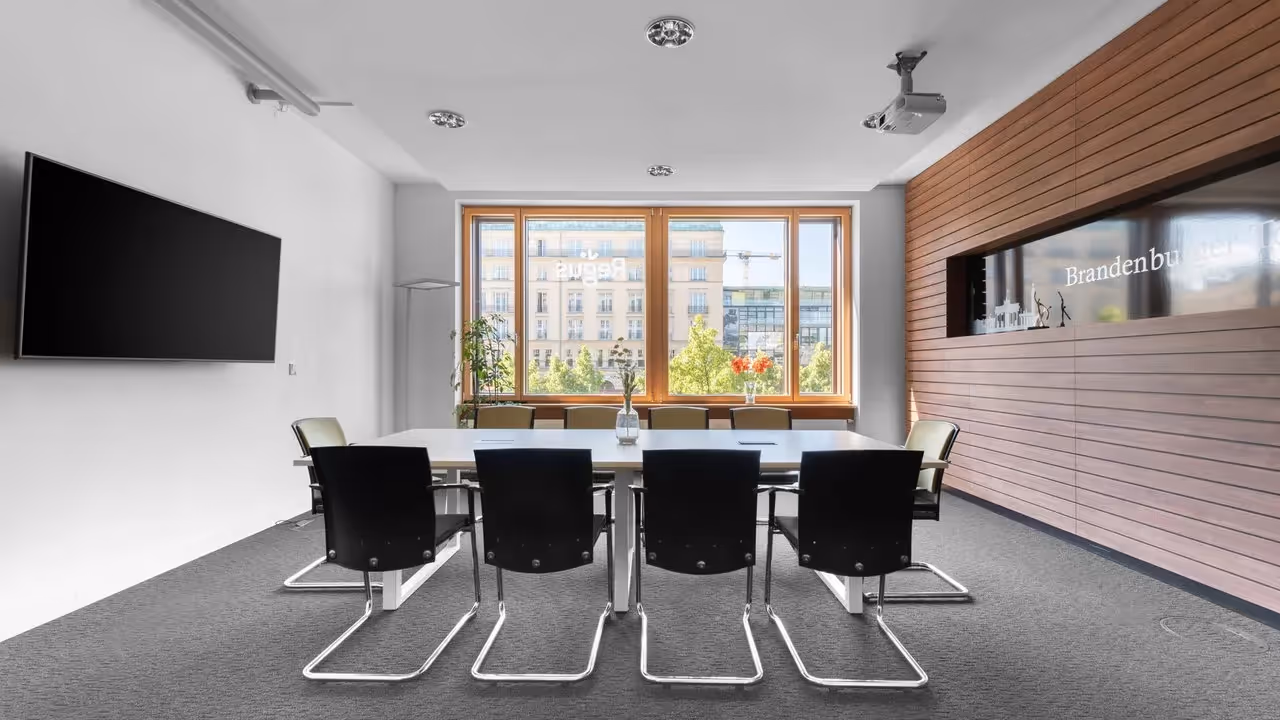 Konferenzraum mit großem Tisch, schwarzen Stühlen, Holzwand, Projektor, großem Fenster, Blick auf Gebäude.