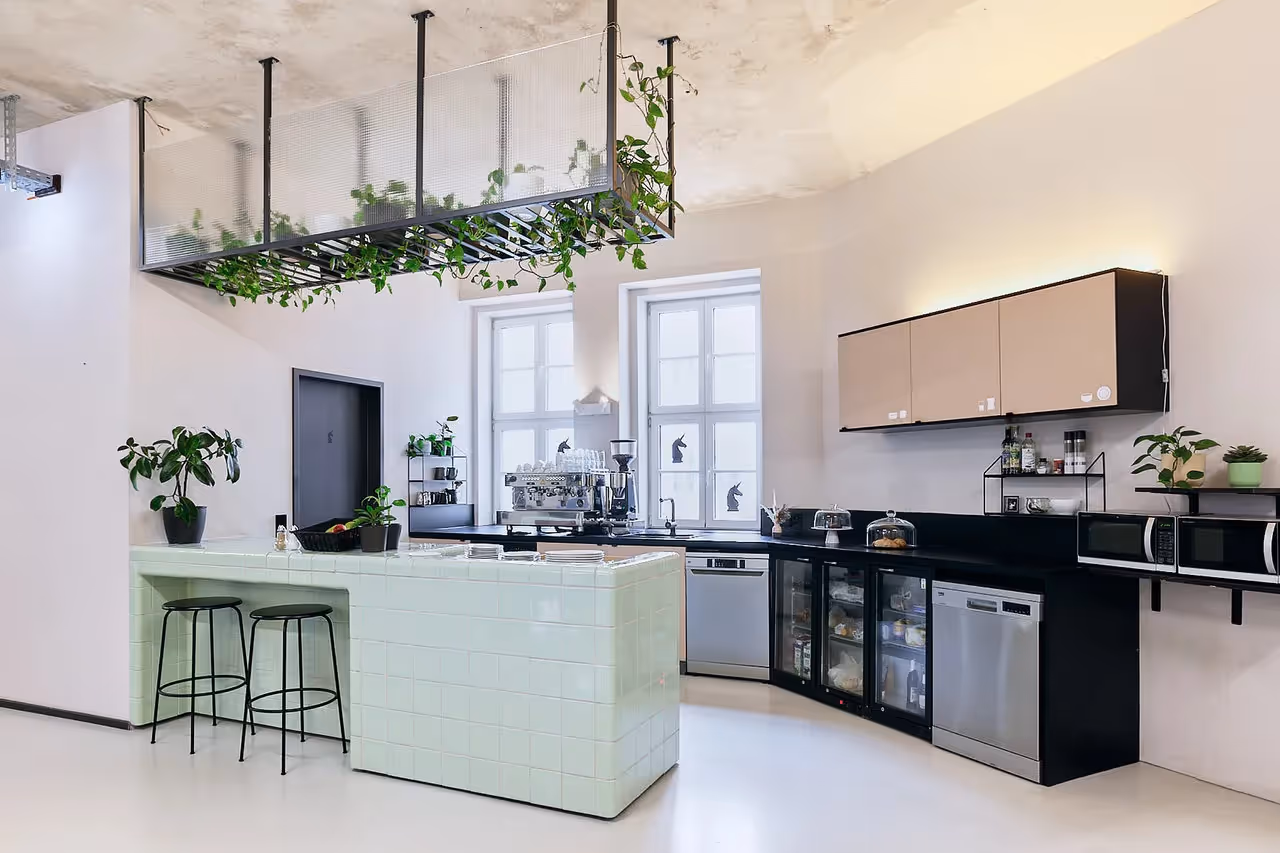 Helle Küche mit mintgrüner Bar, schwarzen Barhockern, Pflanzen, Kühlschrank, Mikrowelle und großen Fenstern.