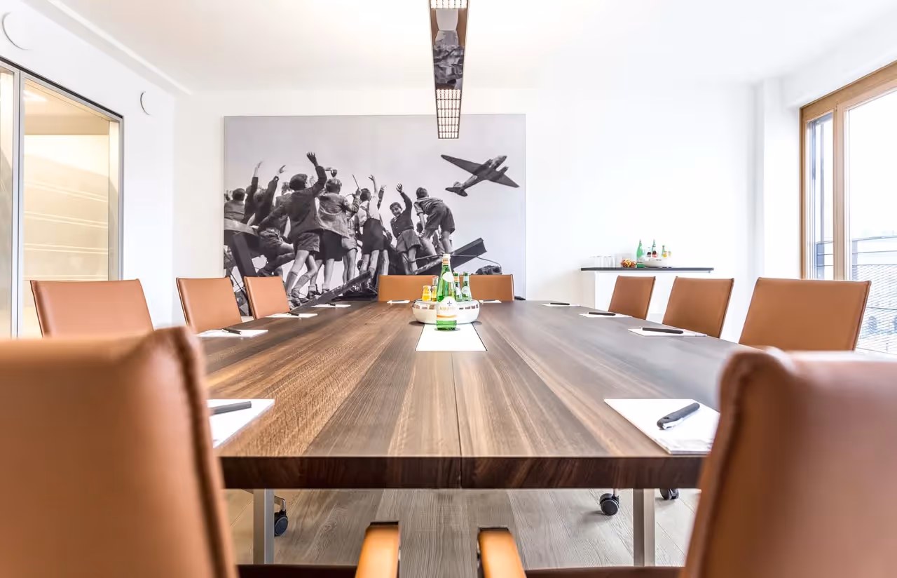 Konferenzraum mit großem Holztisch, braunen Lederstühlen, Wandbild und moderner Beleuchtung.