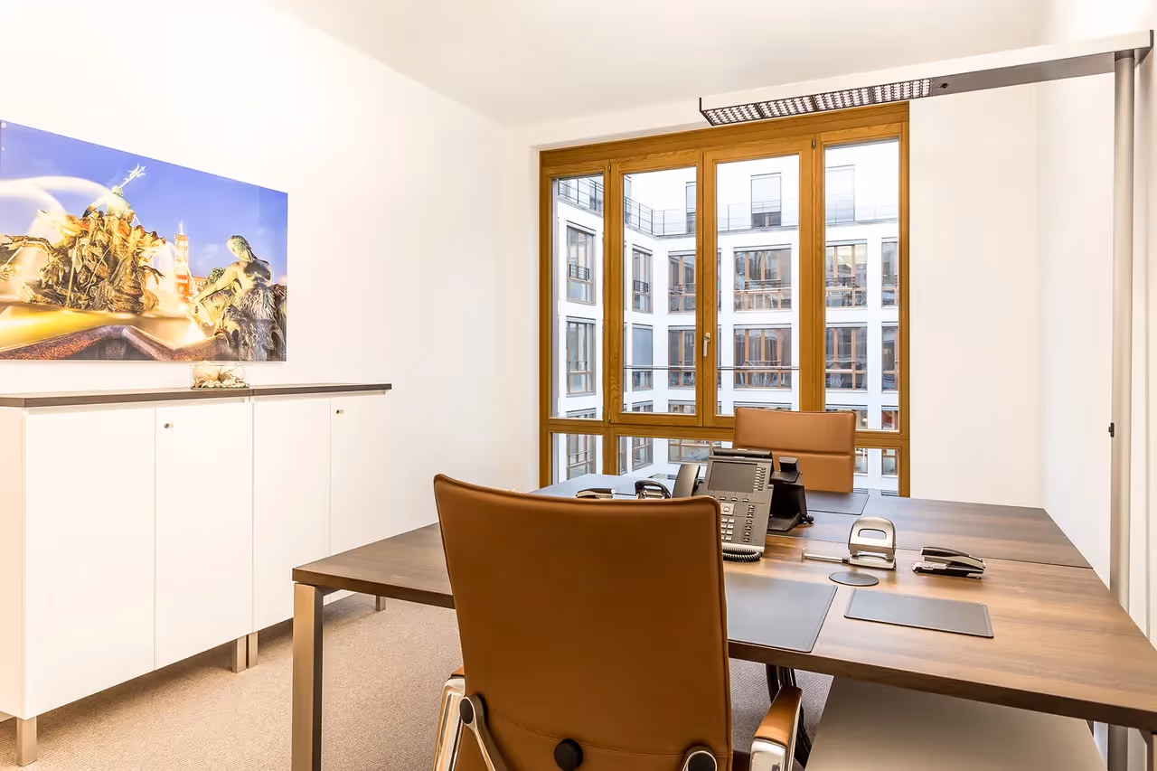 Büro mit Holztisch, braunen Stühlen, Telefon, großem Fenster und Kunstwerk an der weißen Wand.