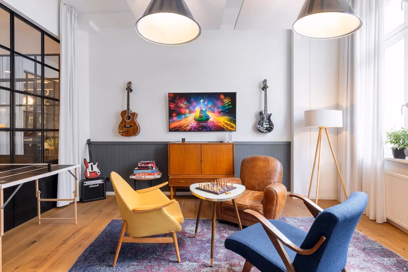 Wohnbereich mit Retro-Möbeln, Gitarren an der Wand, Flügeltür, Tischlampe, Teppich und großem Fenster.