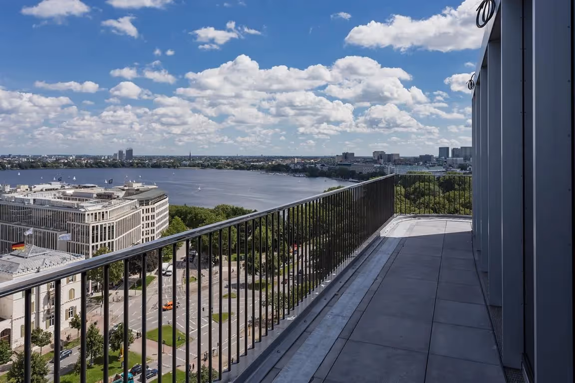 Dachterrasse mit Blick auf Fluss, Gebäude und Stadtlandschaft, blauer Himmel mit Wolken.