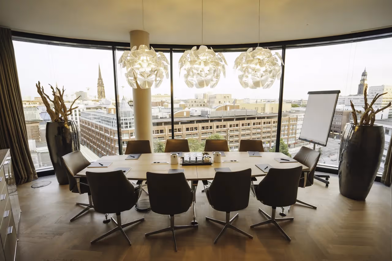 Großer Konferenztisch mit Ledersesseln, hölzerner Boden, große Fenster mit Stadtblick, moderne Hängelampen.