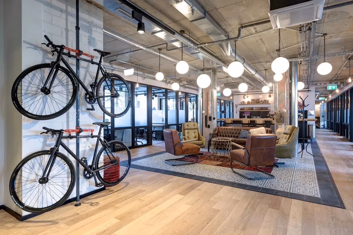Helle Lounge mit Ledersofas, Fahrrädern an der Wand, hängenden Kugelleuchten und Holzboden.