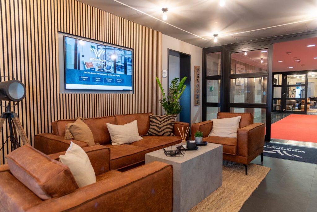 Lounge mit braunen Ledersofas, Holzwand, großem Bildschirm, Beton-Couchtisch, Pflanzen, und moderner Beleuchtung.