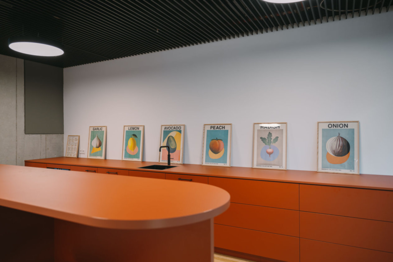 Orangene Küchenzeile mit schwarzen Armaturen, Frucht- und Gemüseposter an der Wand, moderne Beleuchtung.