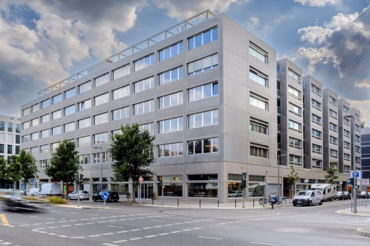 Sechsstöckiges Bürogebäude mit großen Fenstern, Bäumen davor, und einer belebten Straßenecke.