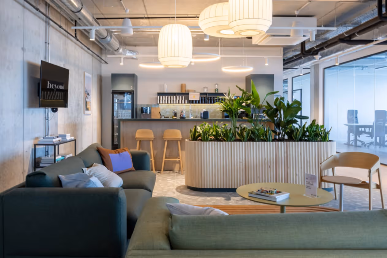 Gemütlicher Lounge-Bereich mit Sofas, Pflanzen, Bar, Holzstühlen und großer Hängelampe in offenem Coworking-Space.