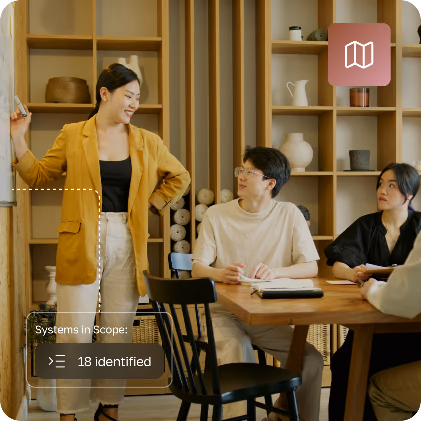 Three people in a meeting room, one standing by a whiteboard and two seated at a wooden table, engaged in discussion.