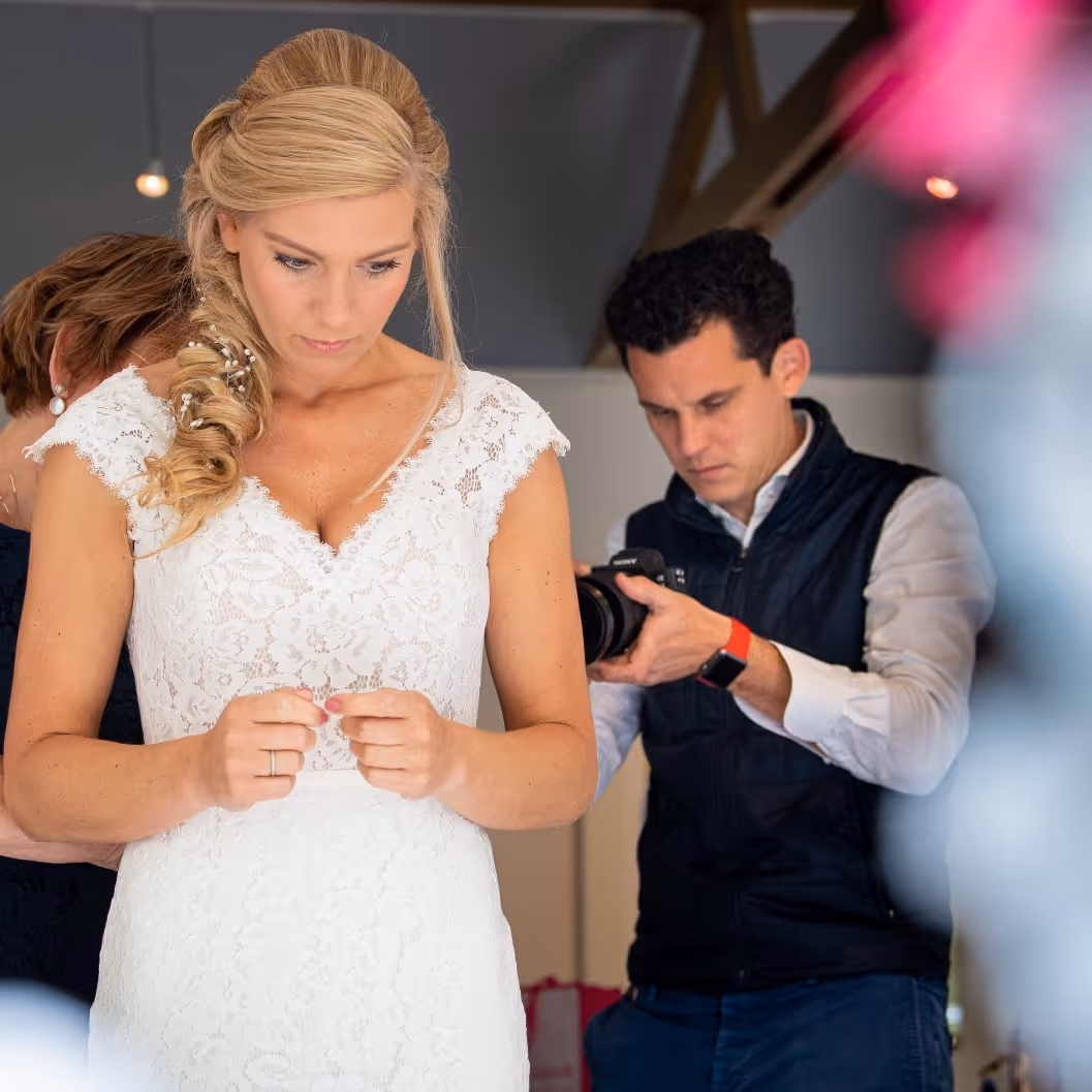Een bruid met achter haar een ander persoon, die wordt gefotografeerd door een fotograaf.
