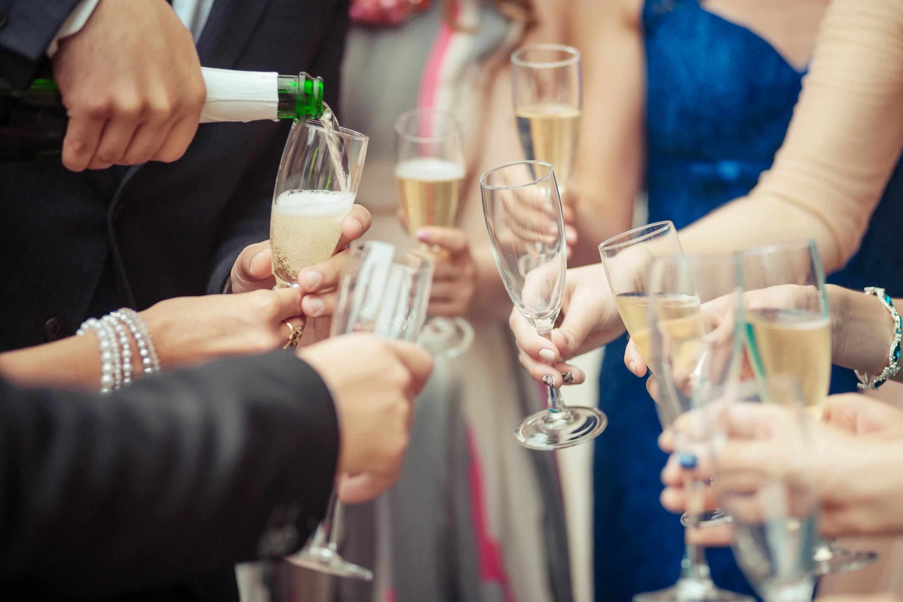 Close-up van een groep mensen in feestelijke kleding die champagneglazen bij elkaar houden. Een persoon schenkt champagne in de glazen.