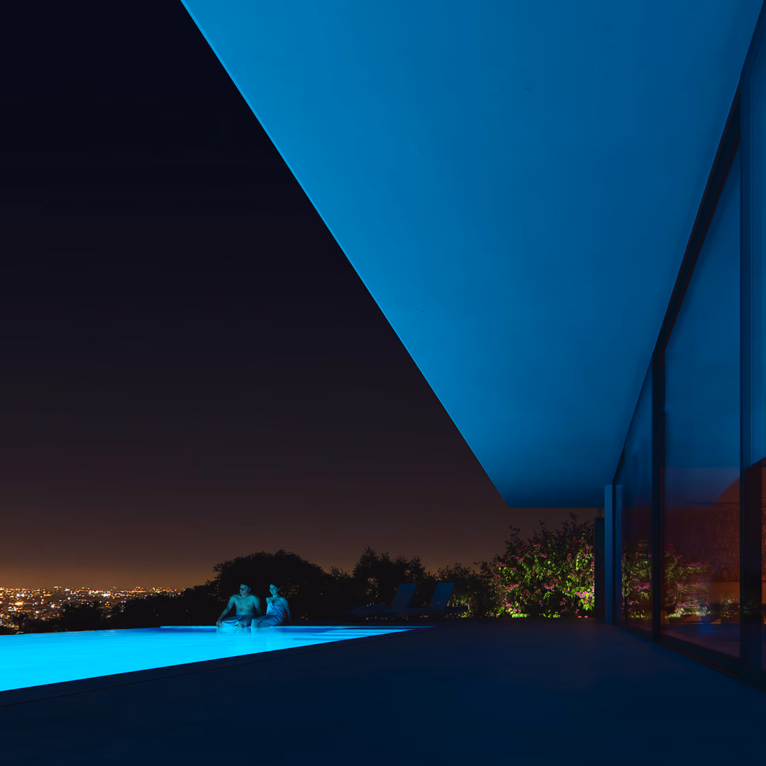 Architectural visualization of a modern villa in Portugal, featuring a minimalist design with a sleek infinity pool illuminated in blue. The floor-to-ceiling glass façade reflects the night sky, blending the indoor and outdoor spaces. A high-end render showcasing luxury residential architecture and atmospheric lighting.