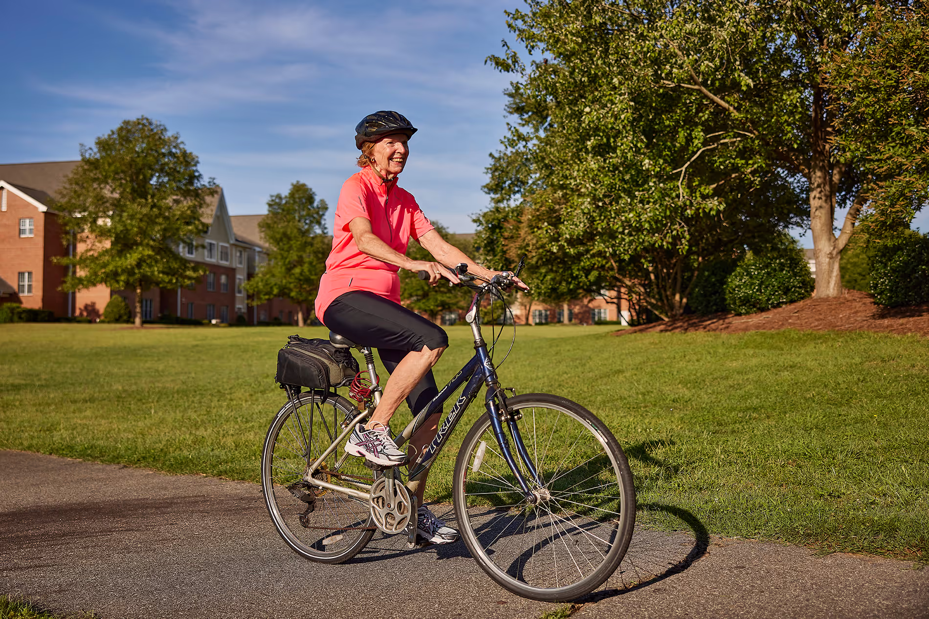 A woman wearing a helmet rides a bicycle on a path in a park.