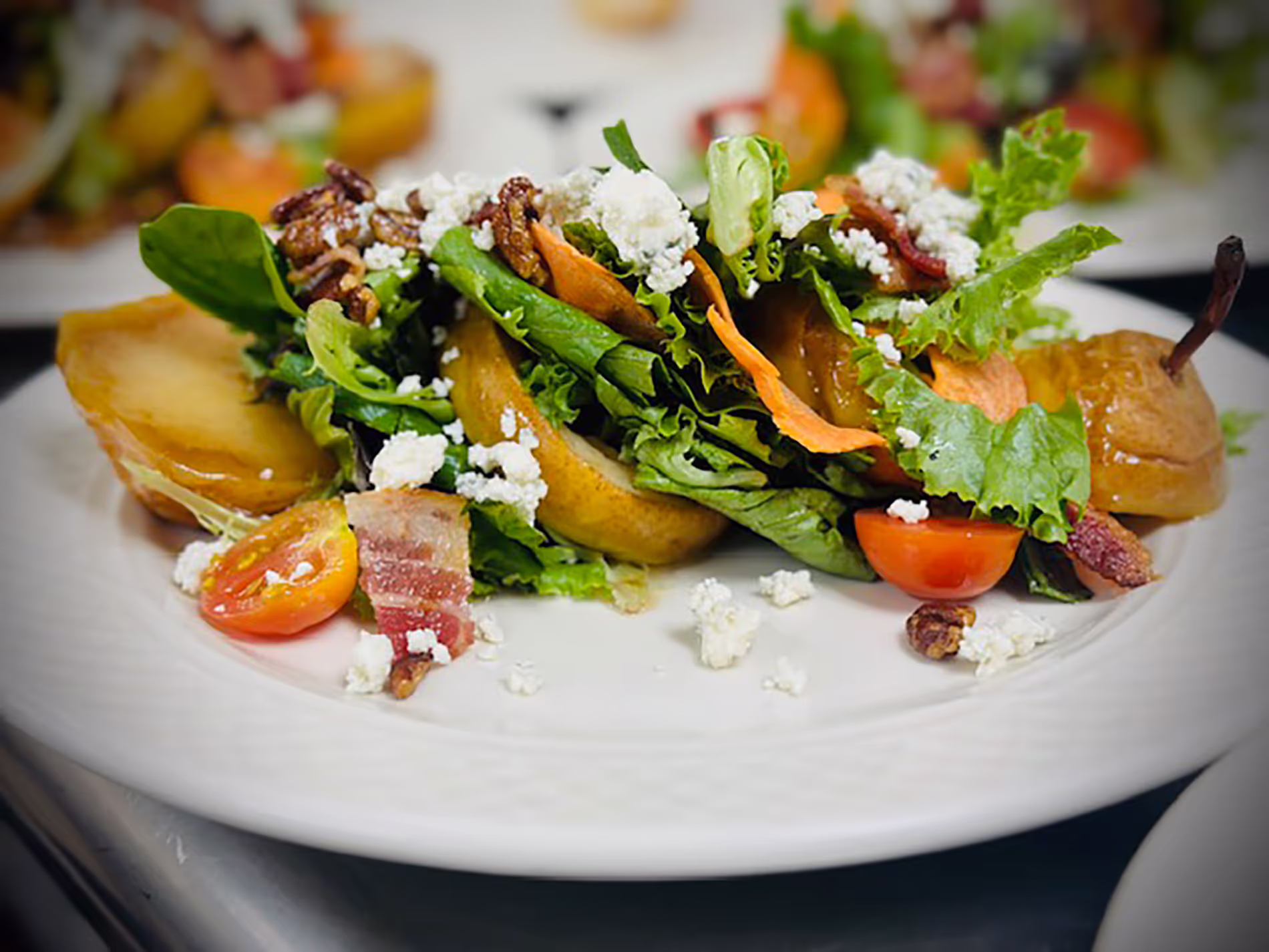 A fresh salad with lettuce, cherry tomatoes, bacon, and crumbled cheese on a white plate.