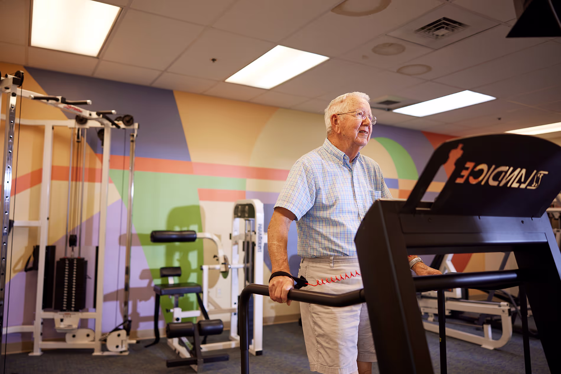 An elderly man exercises on a treadmill in a gym.