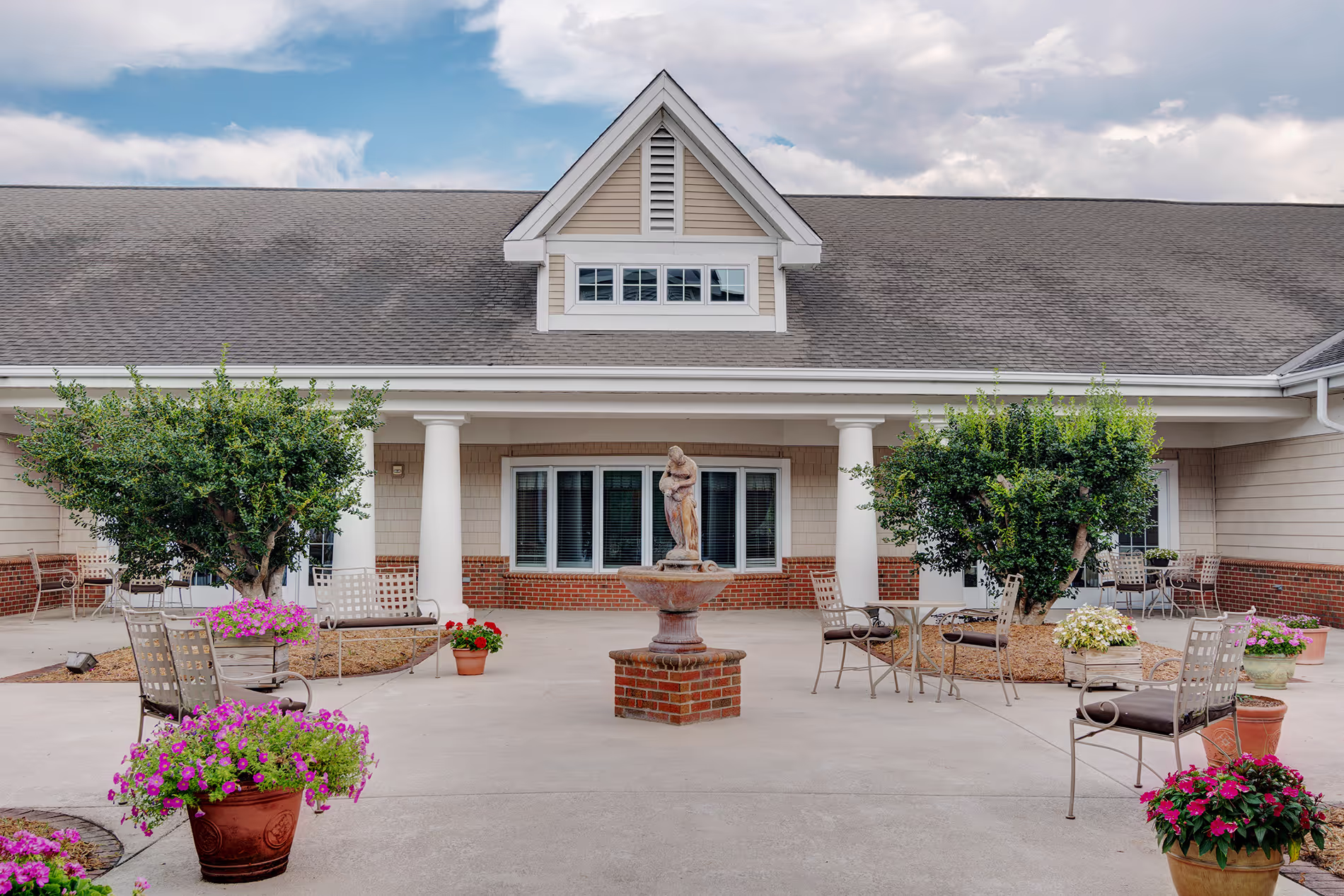Outdoor courtyard with a central fountain surrounded by chairs and colorful flower pots.