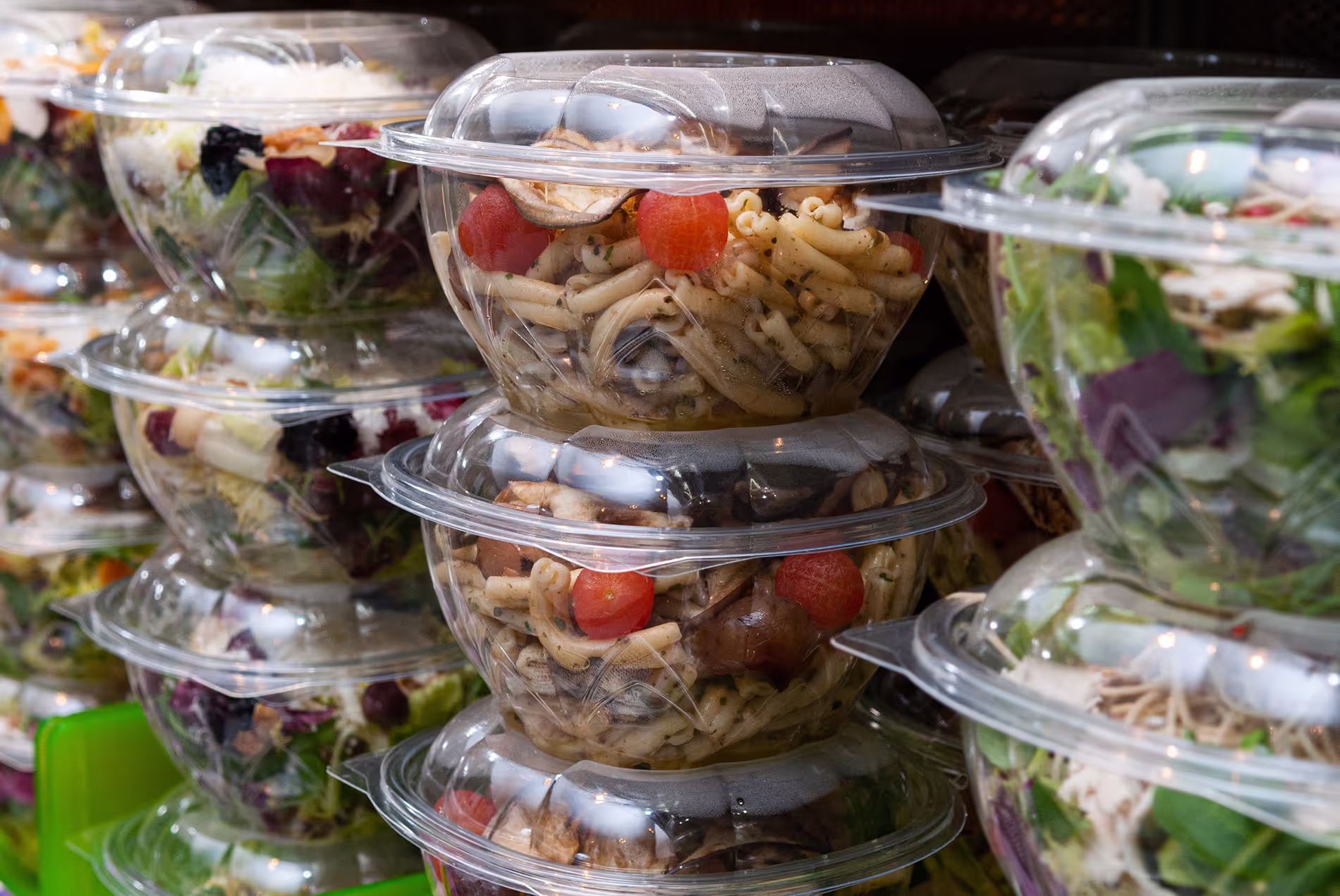 Stacked plastic containers filled with pasta and salad in a refrigerator display.