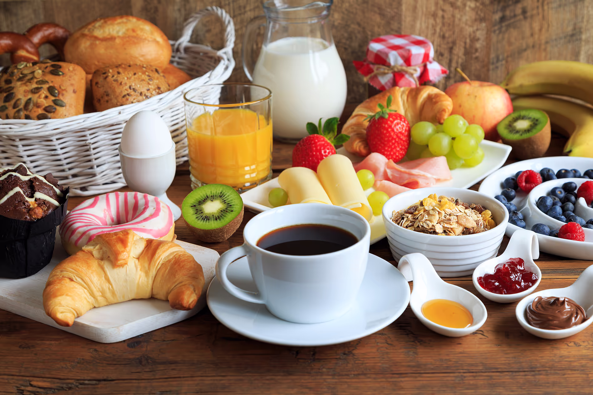 A breakfast spread with coffee, croissants, fruit, yogurt, juice, and various breads on a table.