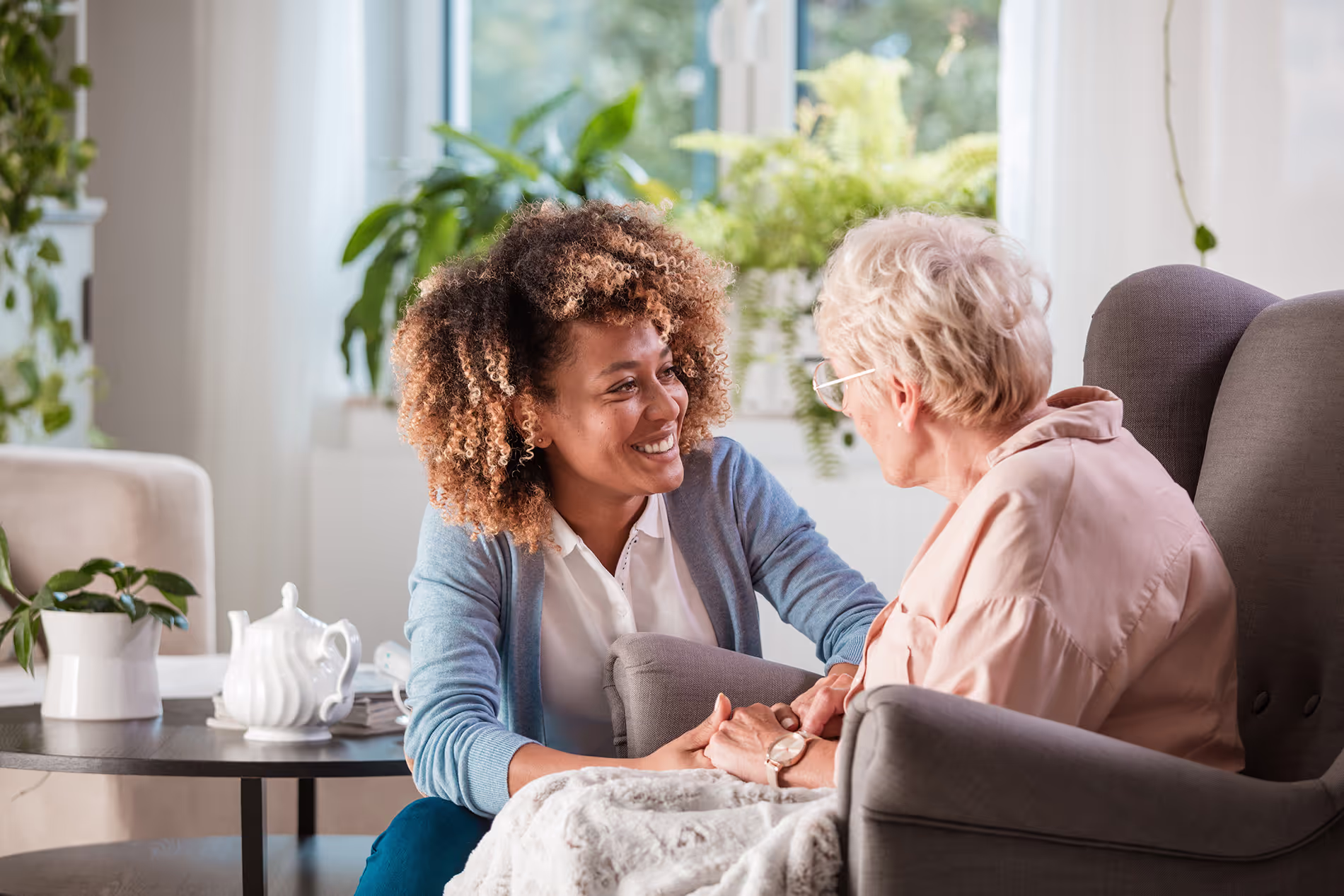 A young woman smiles while talking to an older woman seated in a comfortable chair.