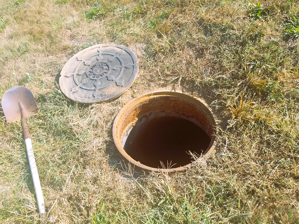 Shovel and manhole lid laying on ground next to an open manhole